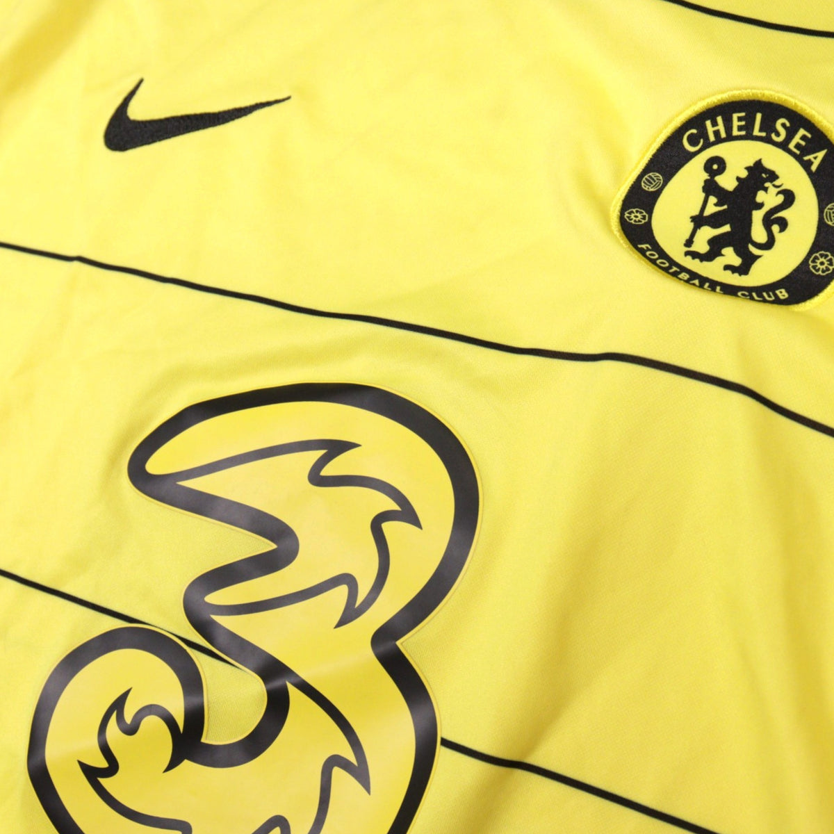 Close-up of Chelsea crest, Nike swoosh and Three sponsor on the yellow 2021/22 away shirt