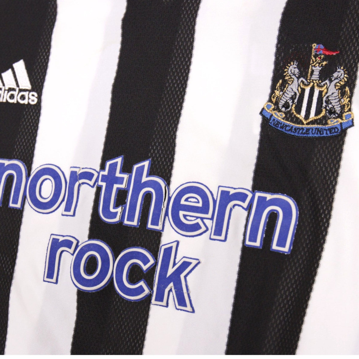 Close-up of adidas logo, Northern Rock sponsor and Newcastle United crest on the shirt
