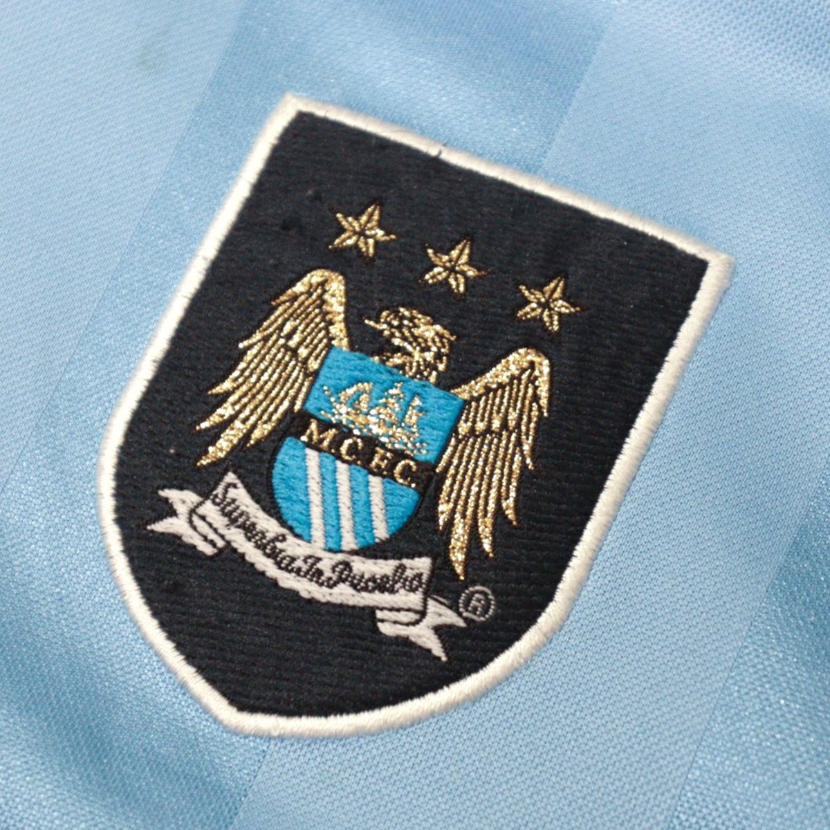Close-up of the embroidered Manchester City crest with three stars and gold eagle