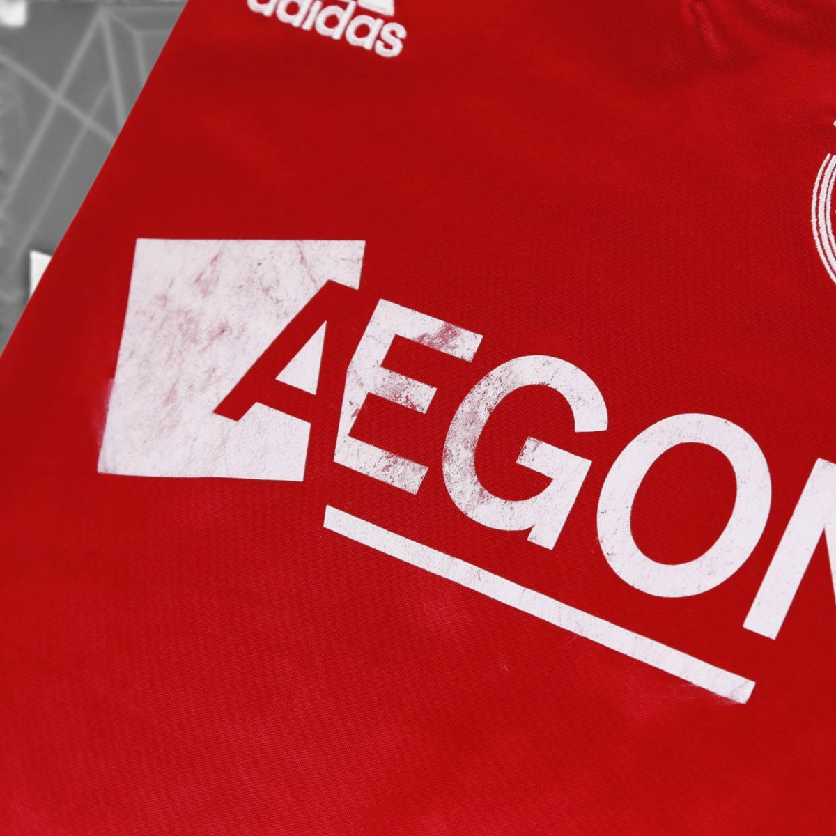 Close-up of the AEGON sponsor print on the Ajax home shirt showing surface wear