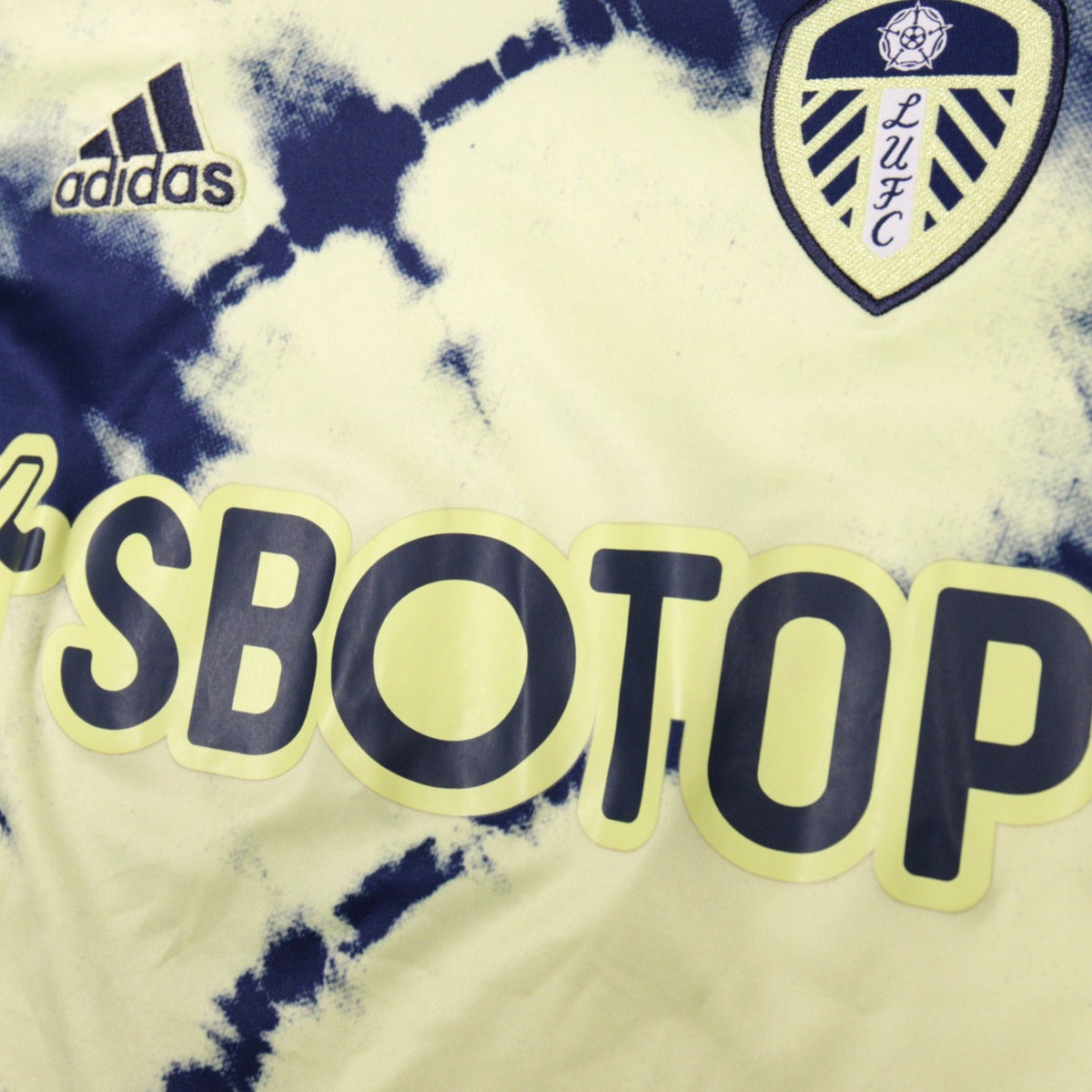 Close-up of adidas logo, Leeds United crest and SBOTOP sponsor on front