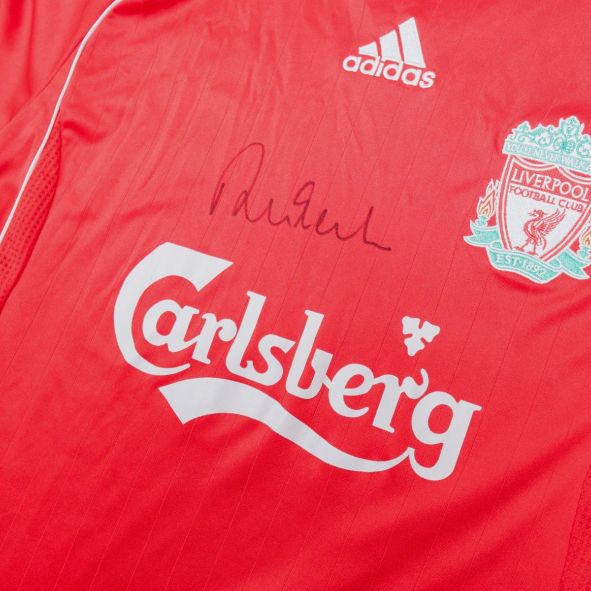 Close-up of the adidas logo, Liverpool crest, Carlsberg sponsor and signature on the chest