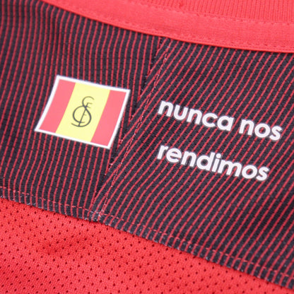 Close-up of Sevilla shirt rear collar showing Spanish flag badge and 'nunca nos rendimos' slogan