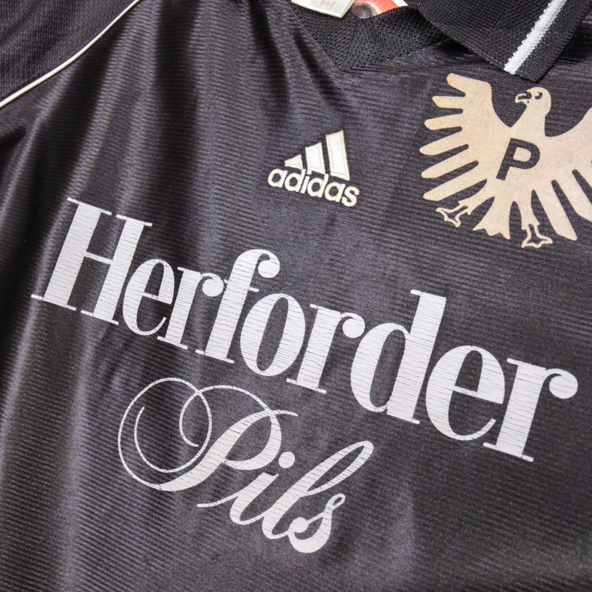 Close-up of chest print showing Herforder Pils sponsor, adidas logo, and eagle crest