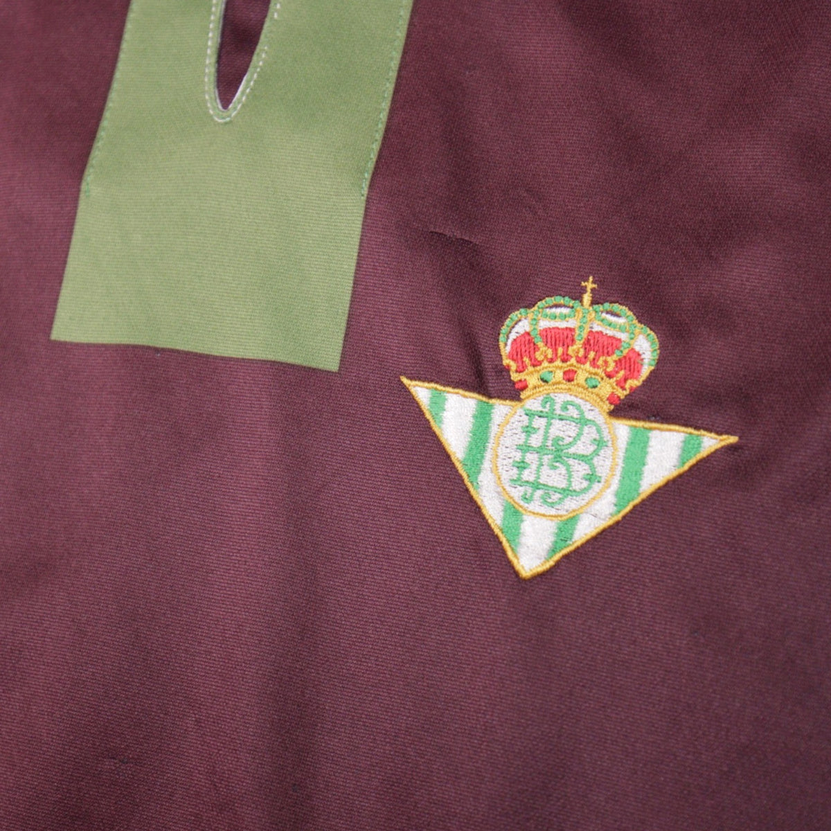 Close-up of the Real Betis crest and green v-neck placket
