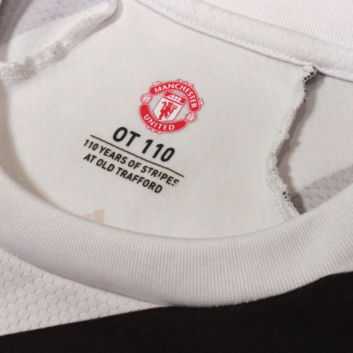 Close-up of the neck label reading OT 110, 110 Years of Stripes at Old Trafford