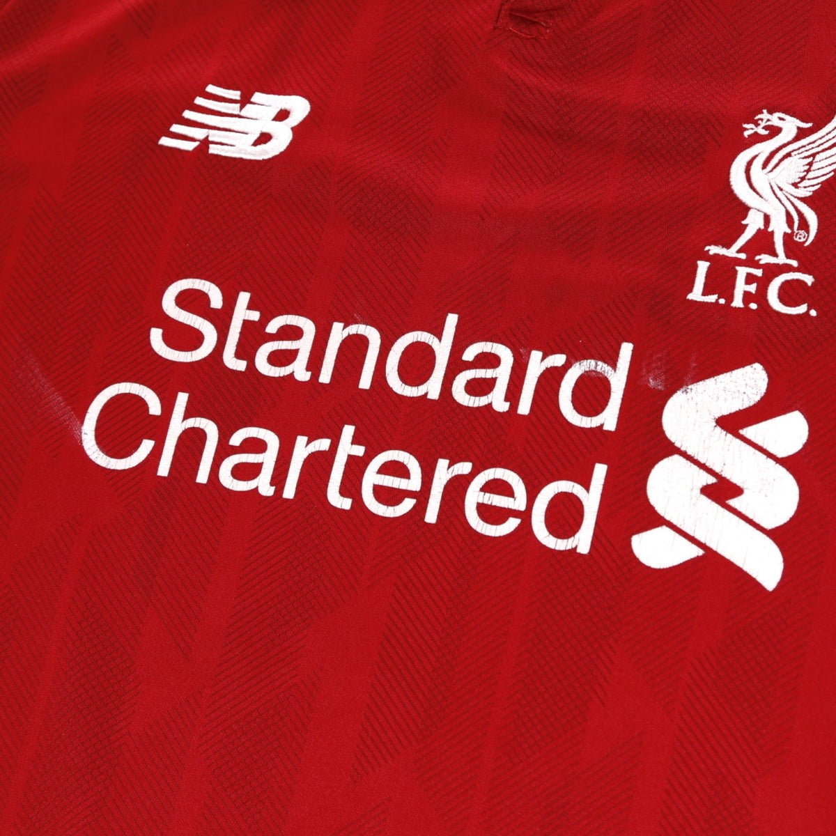 Close-up of the New Balance logo, Liverpool crest and Standard Chartered sponsor on the chest