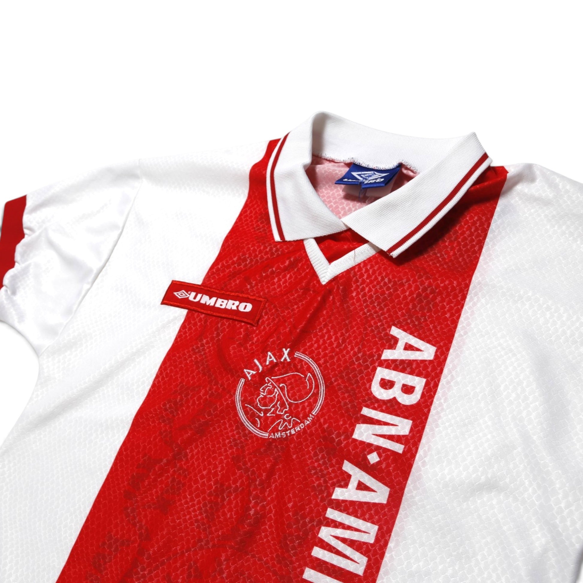 Close-up of Ajax crest, Umbro logo, and ABN·AMRO sponsor on collar area